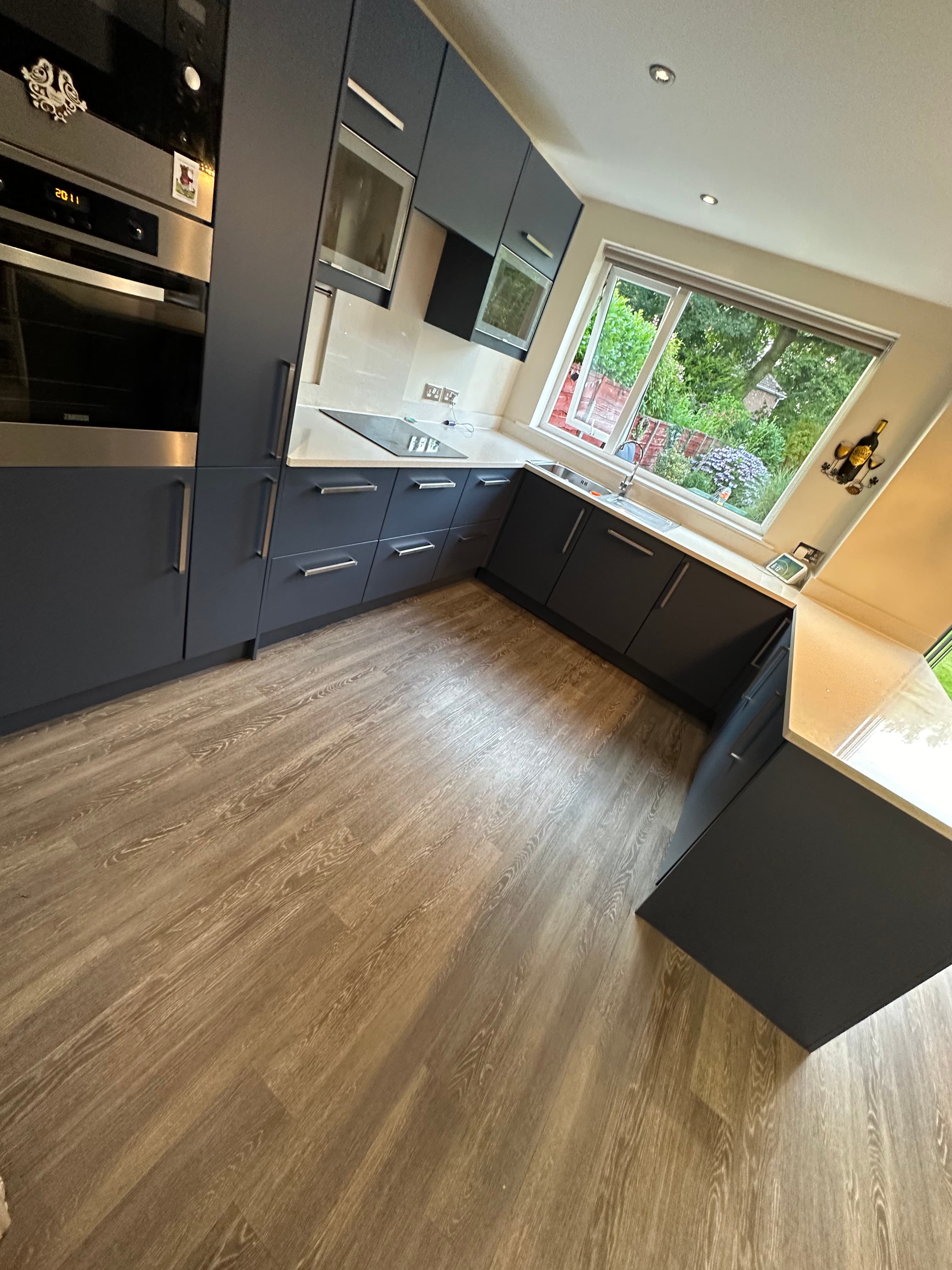 Before and after of a Howdens kitchen respray in Urmston — cabinets in deep navy with brass handles
